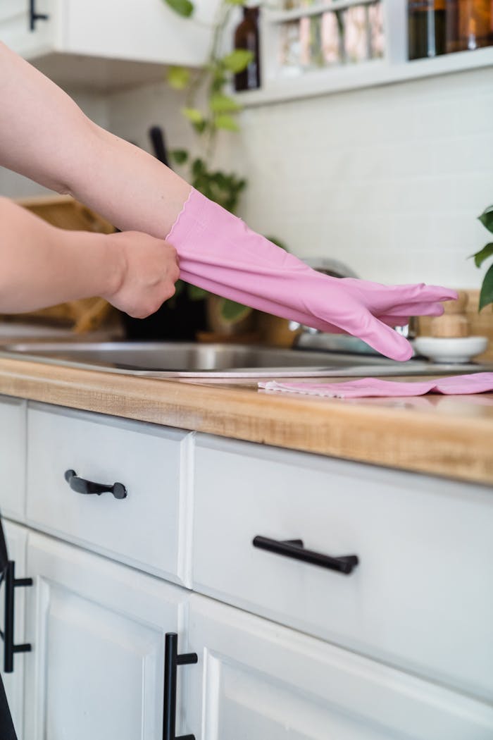 Close-up of hands wearing pink gloves for domestic cleaning in a modern kitchen setting.