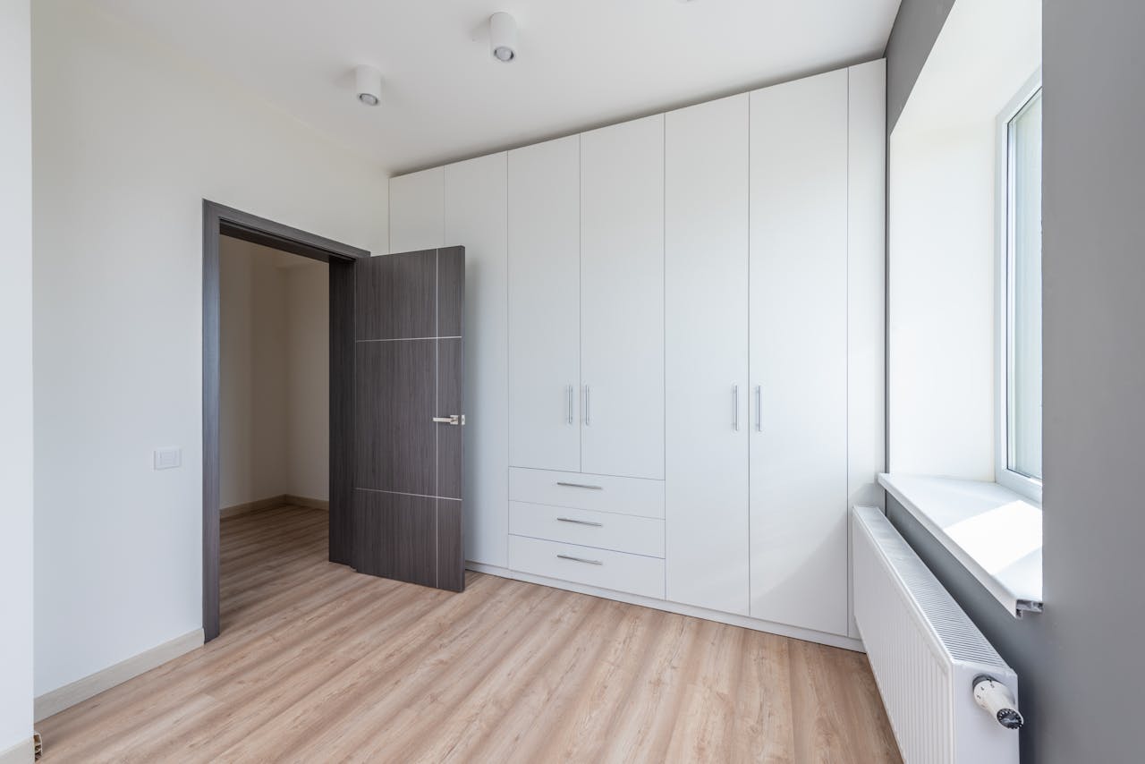 A bright, empty room featuring sleek white cabinets and wooden flooring, ideal for interior design concepts.